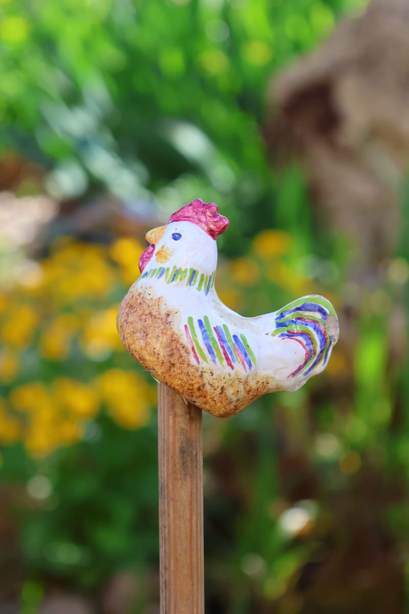 Keramikhuhn als Gartenstecker zwischen Blumen